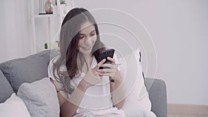 Beautiful Asian woman using smartphone while lying on the couch in her living room. Lifestyle woman at home concept.