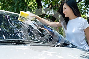 Beautiful Asian woman washing gray car outdoors on vacation
