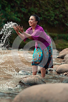 A beautiful Asian woman washing her hand and playing with the water while standing near the river in a traditional purple dress