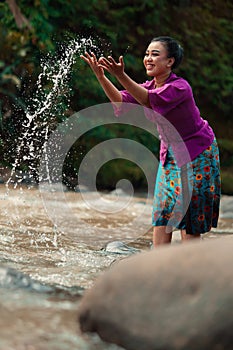 A beautiful Asian woman washing her hand and playing with the water while standing near the river in a traditional purple dress