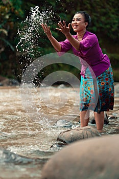 A beautiful Asian woman washing her hand and playing with the water while standing near the river in a traditional purple dress