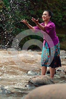 A beautiful Asian woman washing her hand and playing with the water while standing near the river in a traditional purple dress