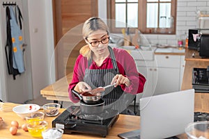 Beautiful asian woman watching recipe for cooking the chocolate cake on laptop in the kitchen room