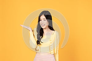 Beautiful Asian woman wearing casual clothes smile and pointing finger to an empty palm isolated on yellow background studio