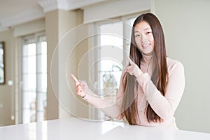 Beautiful Asian woman wearing casual sweater on white table smiling and looking at the camera pointing with two hands and fingers