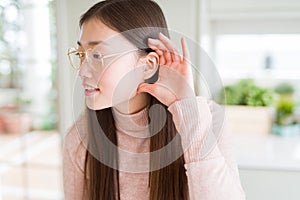 Beautiful Asian woman wearing glasses smiling with hand over ear listening an hearing to rumor or gossip