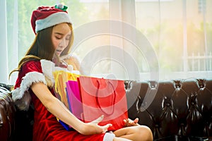 Beautiful asian woman wearing hat and red Santa Claus outfit,sitting on brown leather sofa,enjoy shopping online with tablet,