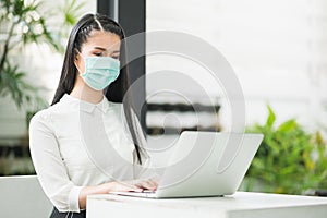 Beautiful asian woman wearing protection mask work from home in the morning. Young asian female with laptop stay at home