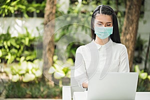 Beautiful asian woman wearing protection mask work from home in the morning. Young asian female with laptop stay at home