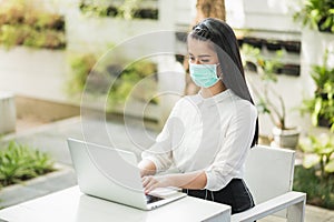 Beautiful asian woman wearing protection mask work from home in the morning. Young asian female with laptop stay at home