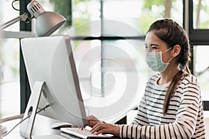 Beautiful asian woman wearing protection mask work from home in the morning. Young asian female working with computer stay at home