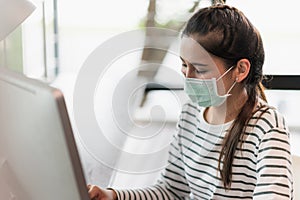 Beautiful asian woman wearing protection mask work from home in the morning. Young asian female working with computer stay at home