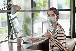 Beautiful asian woman wearing protection mask work from home in the morning. Young asian female working with computer stay at home