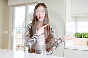 Beautiful Asian woman wearing stripes sweater amazed and smiling to the camera while presenting with hand and pointing with finger