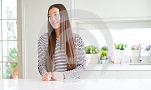 Beautiful Asian woman wearing stripes sweater looking away to side with smile on face, natural expression