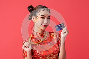 Beautiful Asian woman wearing traditional cheongsam qipao dress showing credit card and gold necklace on red background for
