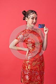 Beautiful Asian woman wearing traditional cheongsam qipao dress showing credit card on red background for Chinese new year