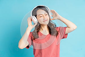 Beautiful asian woman wearing white wireless headphones and holding phone in her hand while dancing to music