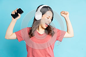 Beautiful asian woman wearing white wireless headphones and holding phone in her hand while dancing to music