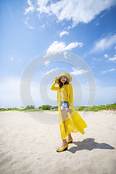 Beautiful asian woman wearing yellow clothes standing on sea beach against midday sun light