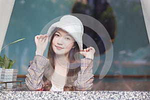 Beautiful Asian woman wears a white hat and plaid coat while she sitting near glassed window in New Year and winter theme photo