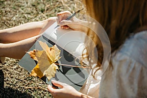 Beautiful asian woman in white dress sit under the tree  writing and thinking in the park with autumn leaves