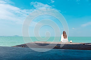 A beautiful asian woman on white dress sitting and looking at the sea and blue sky on wooden balcony