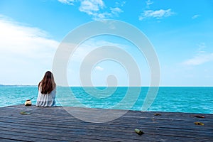 Woman on white dress sitting and looking at the sea and blue sky on wooden balcony with feeling relaxed