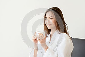 Beautiful Asian woman in white robe holding cup of coffee
