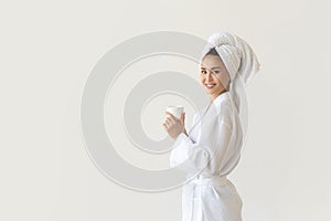 Beautiful Asian woman in white robe and white towel holding cup of coffee, relaxing after taking shower