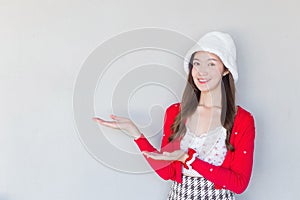 Beautiful Asian woman who wears red coat and white hat as a Santy girl acts her hand to present something and looking at the