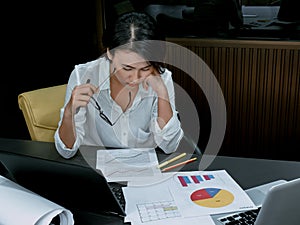 Beautiful Asian woman working overtime with laptop computer on desk in office
