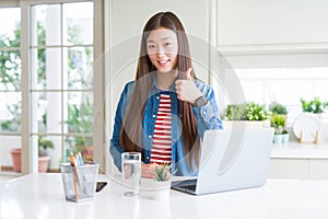 Beautiful Asian woman working using computer laptop doing happy thumbs up gesture with hand