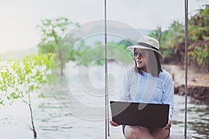 Beautiful asian women sitting and using laptop computer on swing at beach,Happy and smiling,Relaxing time