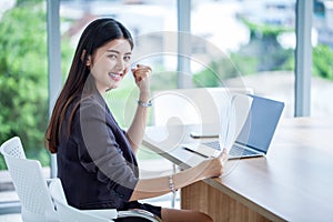 beautiful asian young business woman raised hands celebrating to success achieving goals and hand holding paper document file with