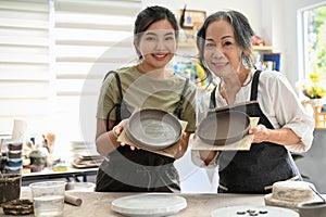 Beautiful Asian young female with an aged woman holding a handmade plate in handicraft workshop