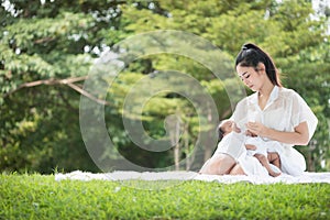 Beautiful Asian young mother  or single mom with new born baby girl are feeding milk from bottle in the park. concept of duties of