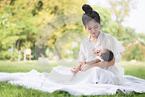 Beautiful Asian young mother  or single mom with new born baby girl are feeding milk from bottle in the park. concept of duties of