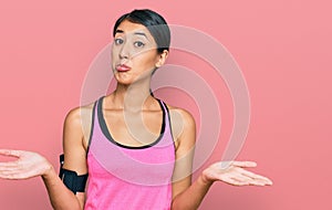 Beautiful asian young sport woman wearing sportswear and arm band clueless and confused expression with arms and hands raised