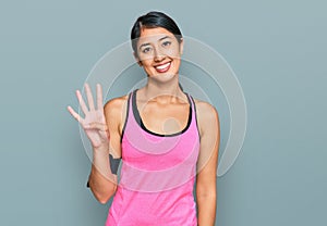 Beautiful asian young sport woman wearing sportswear and arm band showing and pointing up with fingers number four while smiling