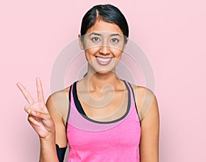 Beautiful asian young sport woman wearing sportswear and arm band showing and pointing up with fingers number two while smiling