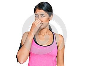 Beautiful asian young sport woman wearing sportswear and arm band smelling something stinky and disgusting, intolerable smell,