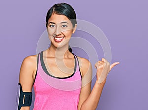 Beautiful asian young sport woman wearing sportswear and arm band smiling with happy face looking and pointing to the side with