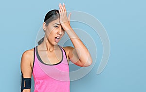 Beautiful asian young sport woman wearing sportswear and arm band surprised with hand on head for mistake, remember error