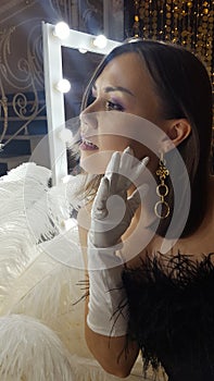 Beautiful asian young woman and decorative ostrich feathers on a gold table next to a make-up mirror. Get ready for the getsby