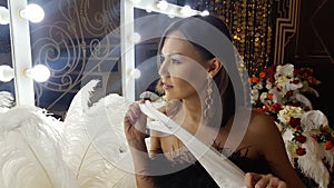 Beautiful asian young woman and decorative ostrich feathers on a gold table next to a make-up mirror. Get ready for the getsby