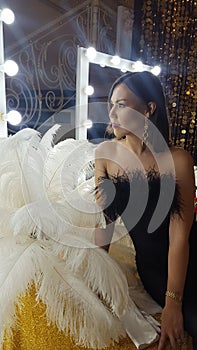 Beautiful asian young woman and decorative ostrich feathers on a gold table next to a make-up mirror. Get ready for the getsby