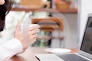 Beautiful asian young woman drink a cup of coffee working online on laptop sitting at coffee shop