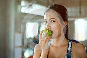 Beautiful Asian young woman eat green apple in fitness gym . healthy eating lifestyle . nutritious . sport . workout. training .