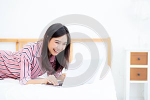 Beautiful asian young woman lying on bed using laptop at bedroom